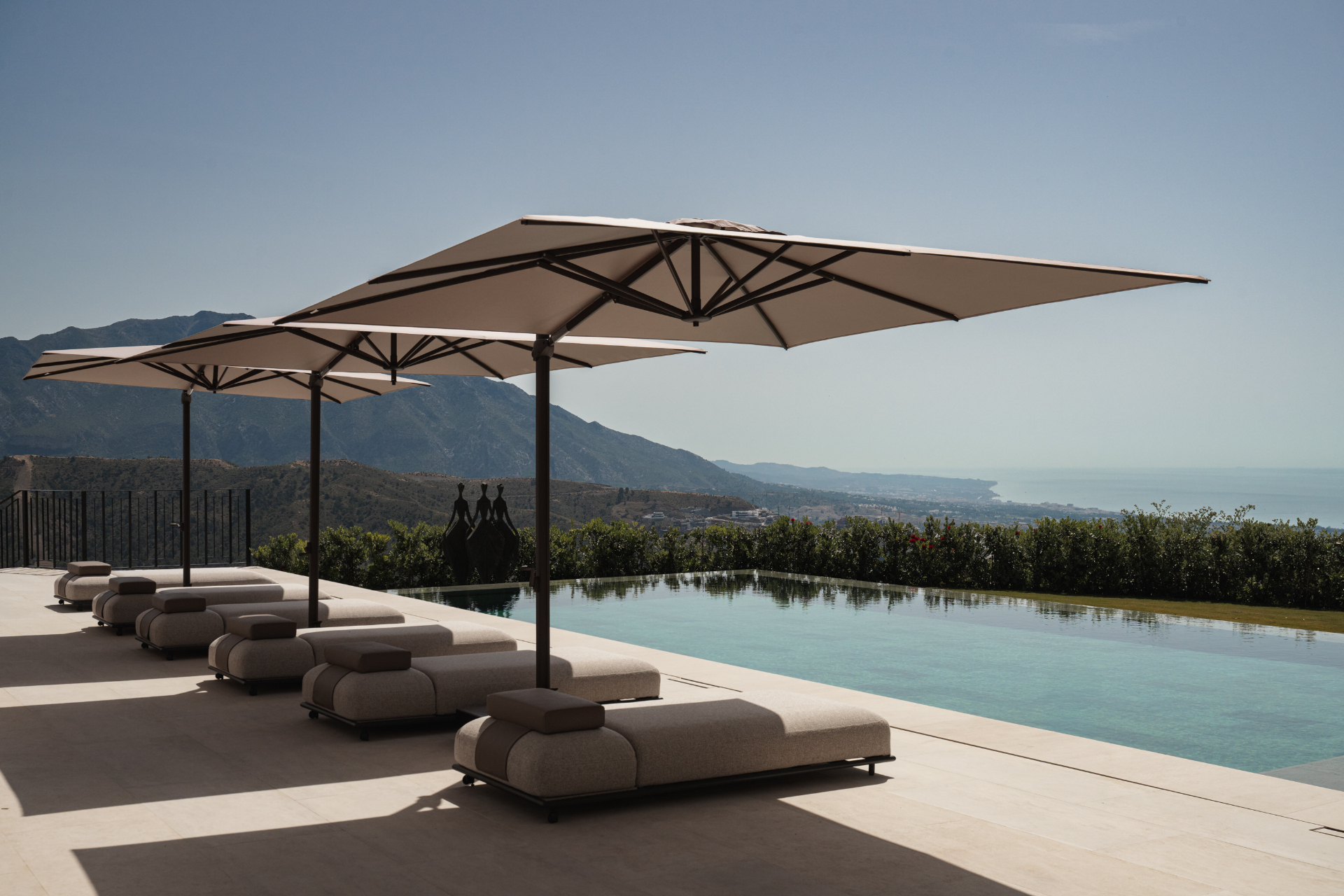 Pool loungers beneath cantilevered parasols above the coast.